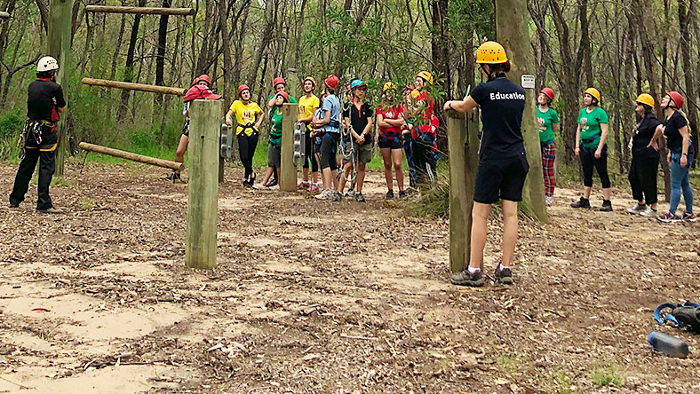 Girls in bush wearing harnesses and helmets taking turns to climb log ladder at Yarramundi NSW