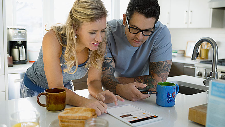 Man and woman at home in kitchen looking over a bill