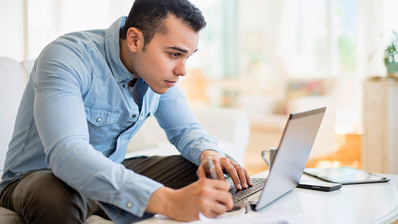 A man in a casual dress shirt and pants using his laptop to set business goals.