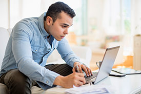 A man in a casual dress shirt and pants using his laptop to set business goals.