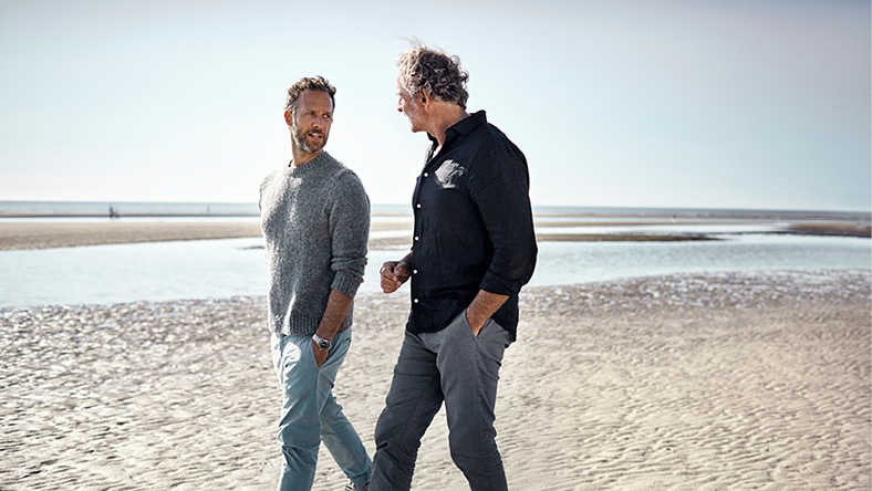 Two men walk along the beach on a sunny day.