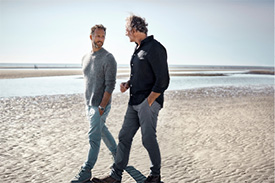 Two men walk along the beach on a sunny day.