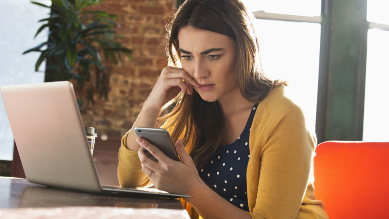 Woman dealing with stress by biting nails at desk as she looks at her mobile phone