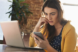 Woman dealing with stress by biting nails at desk as she looks at her mobile phone