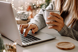 A young woman shops safely on her laptop while clutching a mug of coffee