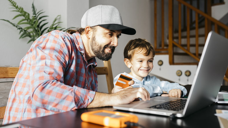 Man comparing credit cards online at home with young boy next to him