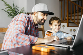 Man comparing credit cards online at home with young boy next to him