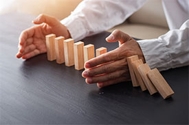 A man using his hand to stop a row of dominoes from falling over.