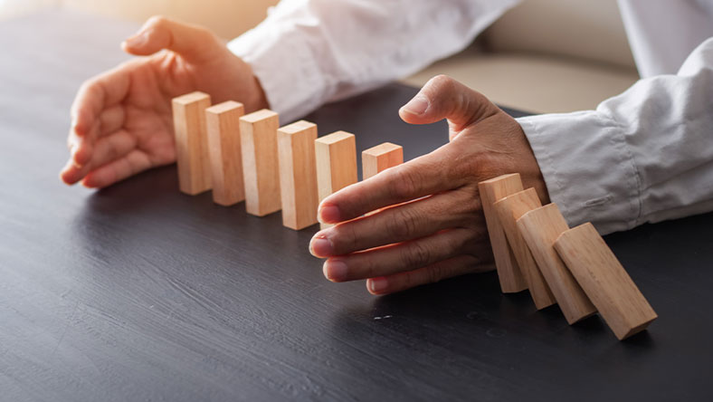 A man using his hand to stop a row of dominoes from falling over.