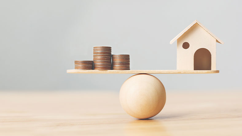 House and coin stacks balancing on board atop wooden ball