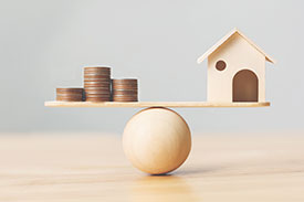 House and coin stacks balancing on board atop wooden ball