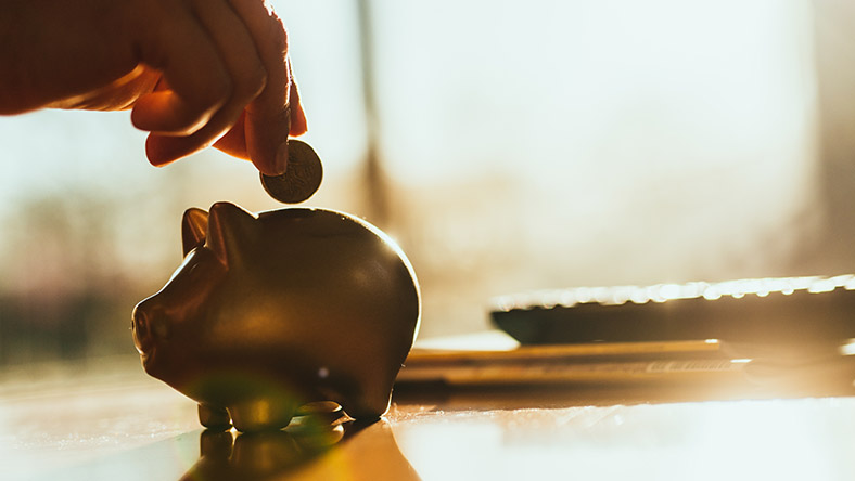 A hand drops a coin into piggy bank.