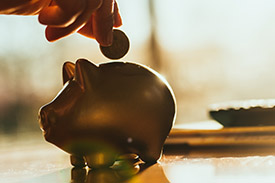 A hand drops a coin into piggy bank.