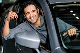 A man with dark hair has his arm out of a new car window holding his car keys.