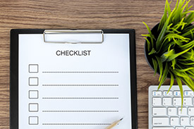 A checklist sits on a desk beside a pot plant and a computer keyboard.