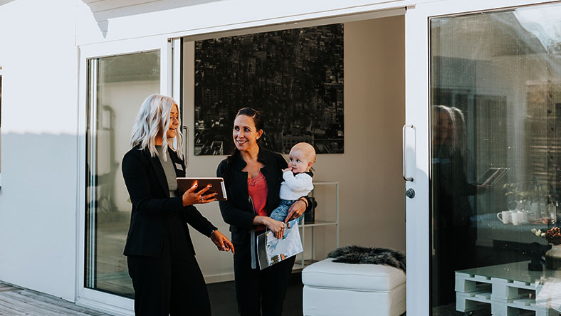 A real estate agent shows a document on an ipad to a young mother and her baby.