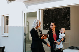 A real estate agent shows a document on an ipad to a young mother and her baby.