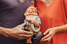A couple hold a garden gnome outside their new home.