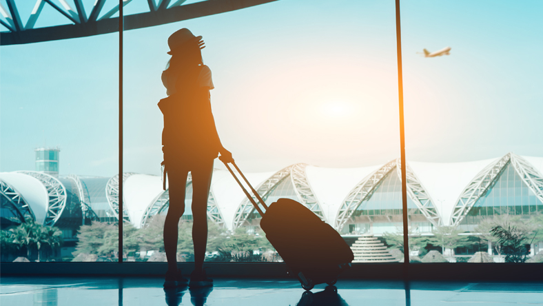 Traveller with suitcase watching planes take off at airport window