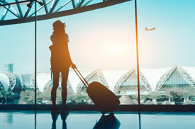 Traveller with suitcase watching planes take off at airport window