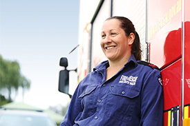 Smiling firefighter leans against fire truck