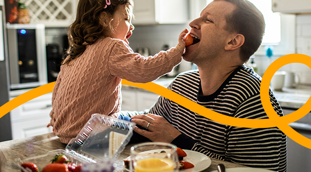 A man plays with his young daughter in their kitchen.