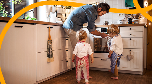 A father cooking in the kitchen with his two small children.