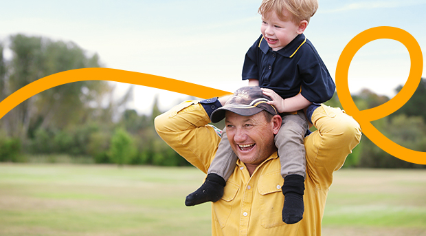 A father carrying his son on his shoulders; both are laughing.