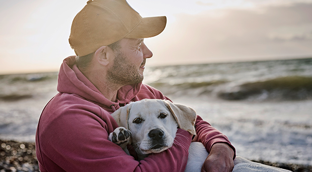 A man holds his dog on the beach at sunrise.