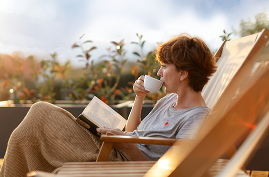 A woman relaxes in a deckchair with a book and cup of tea.