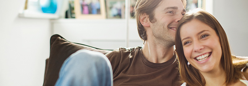 A smiling couple sit on the couch in their new home.