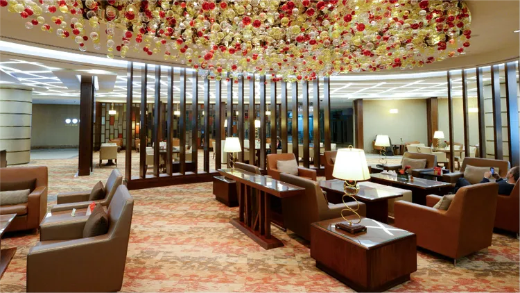 A spacious hotel lounge features plush armchairs and low wooden tables arranged in cozy seating clusters.