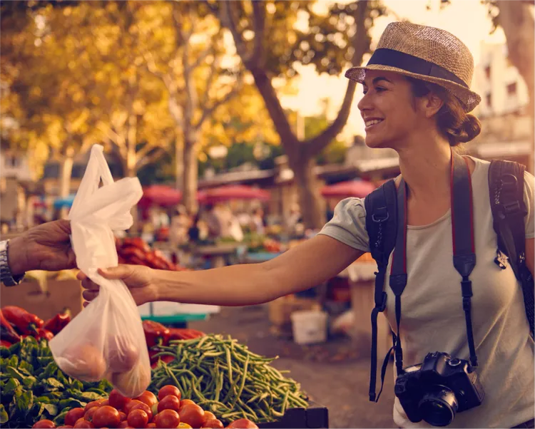 Young woman in a European city takes a bag of fresh fruit and vegetables from a seller.