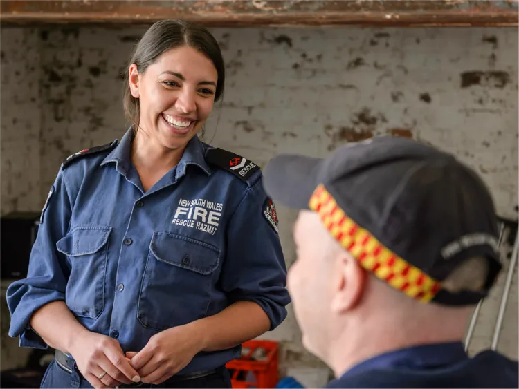 A uniformed fire and rescue worker stands indoors speaking with a colleague.