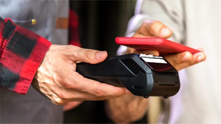 Close-up of a customer paying with a smartphone held over a wireless card reader.